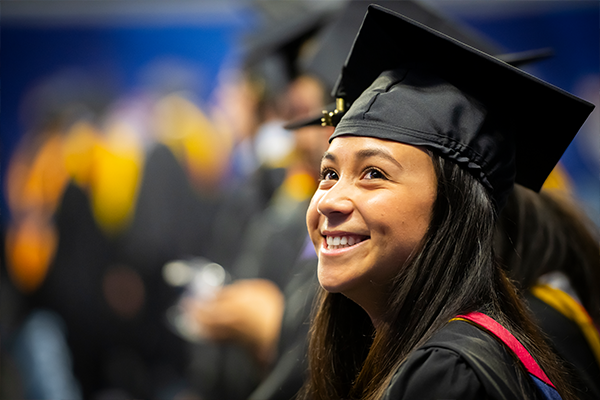 Female student smiling brightly wearing her cap and gown at commencement.