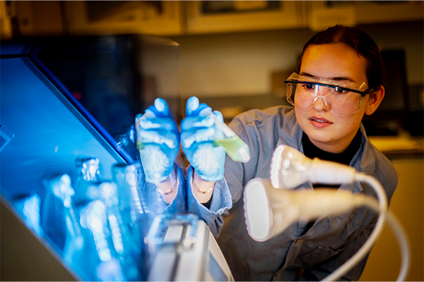 A female student from the Materials Science and Engineering department of Penn Engineering in a lab looking at an object carefully under the light.